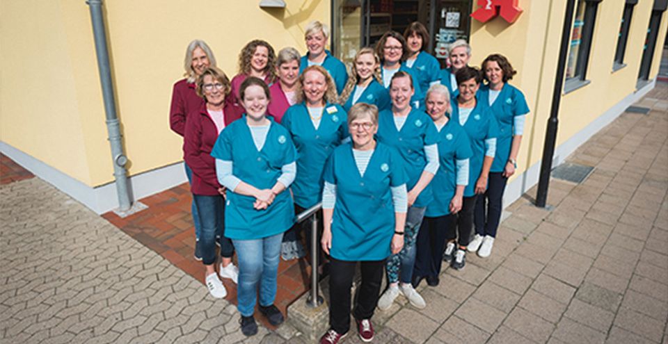 Eine Gruppe von etwa fünfzehn Personen steht draußen vor dem barrierefreien Eingang der Apotheke.